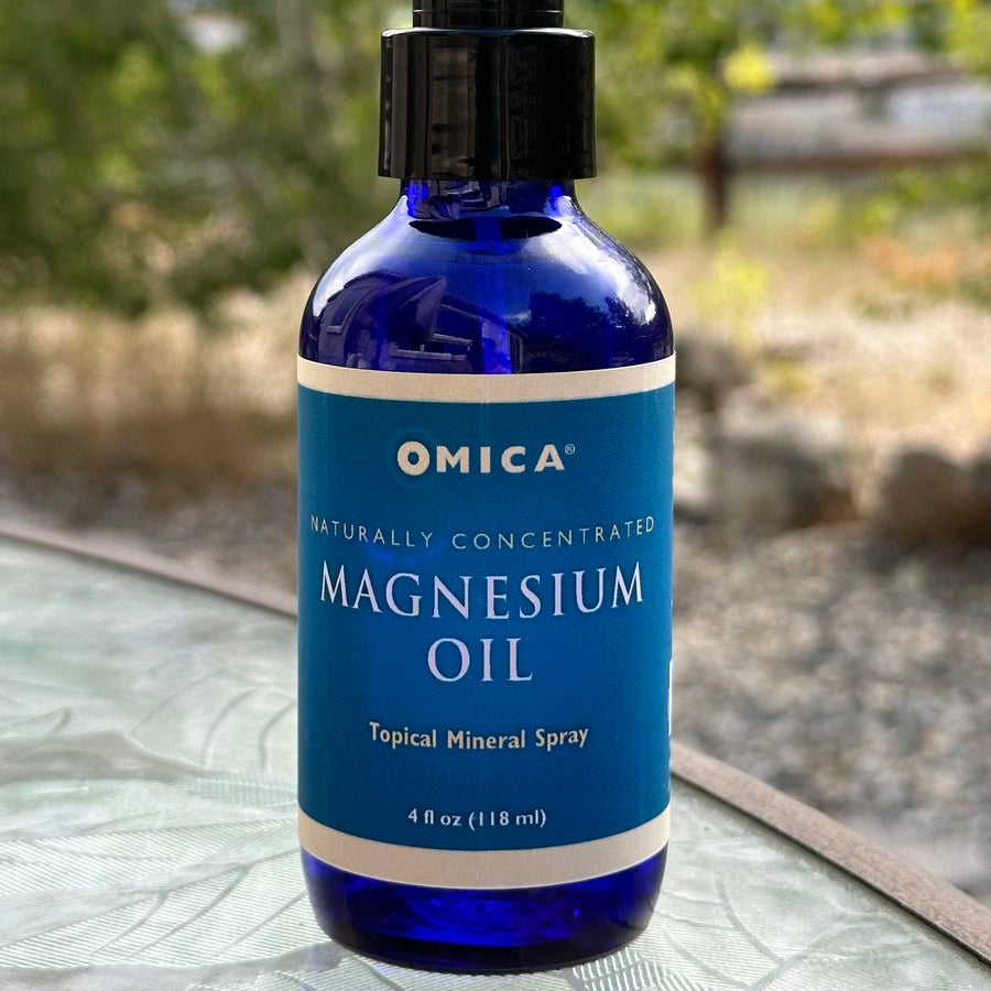Blue bottle of Omica magnesium oil on a glass surface with a blurred outdoor background